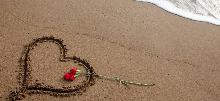 Heart drawn in sand with a flower over
